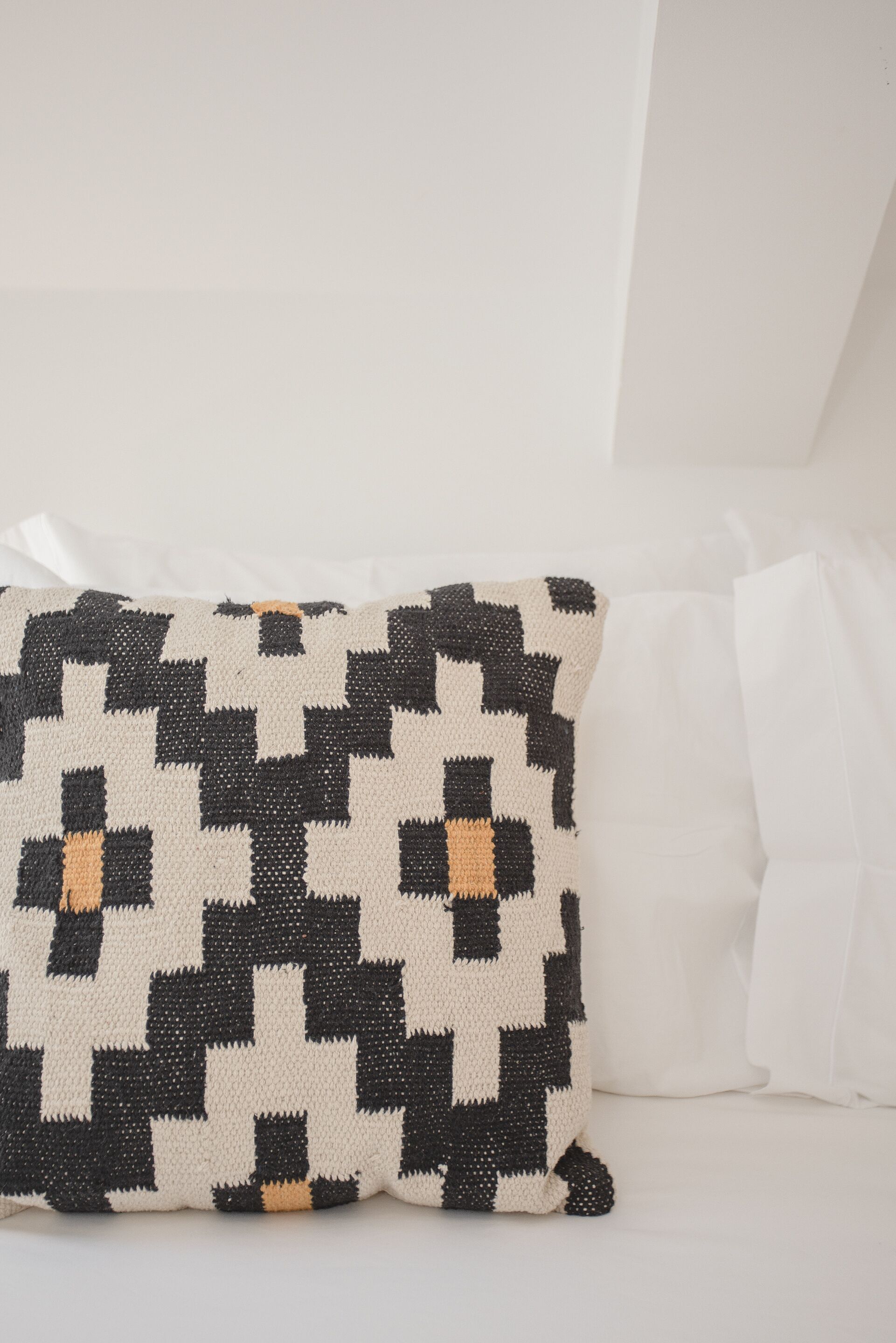 A pillow with a black and white checkered pattern on a white bed.
