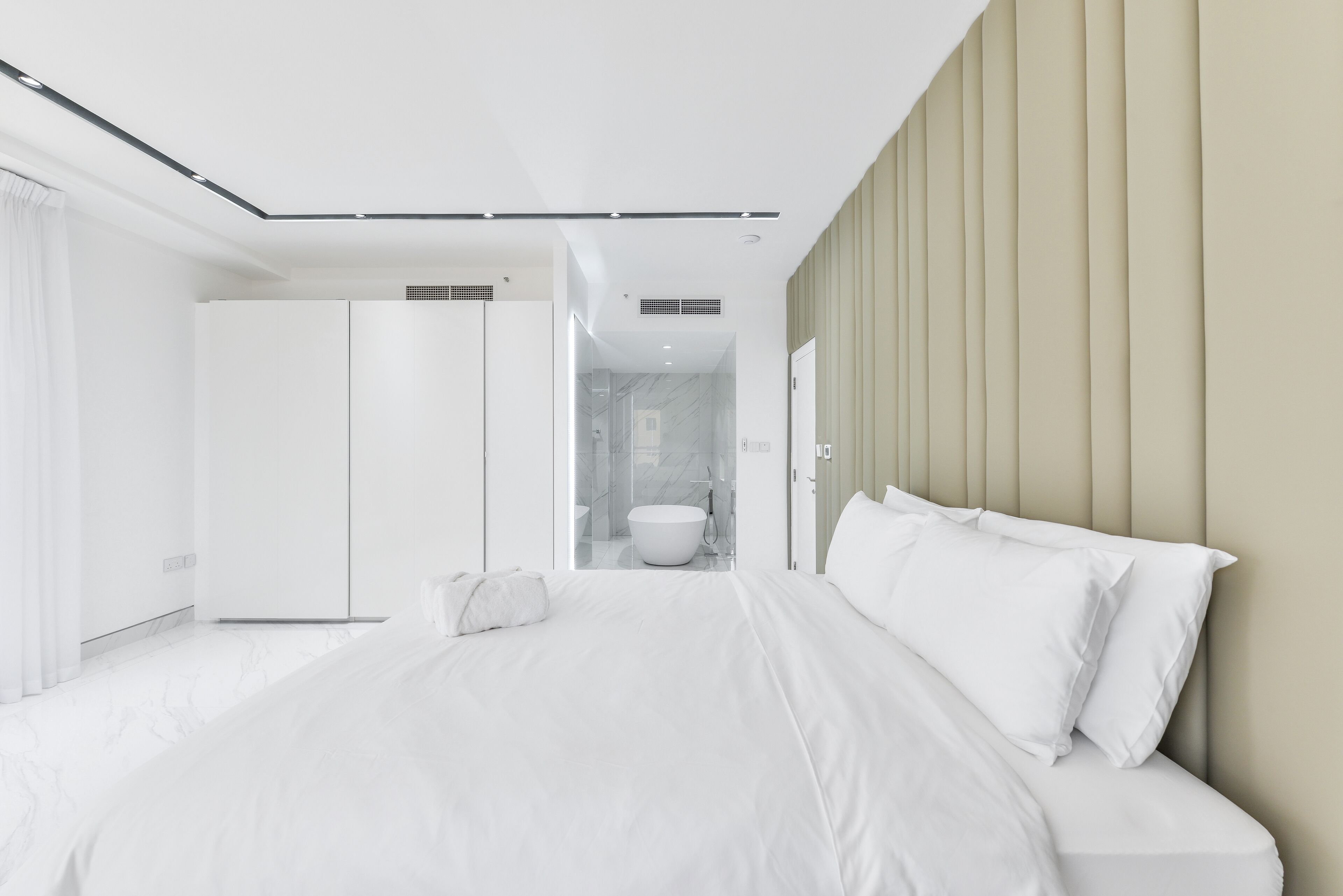 A modern bedroom with a large bed, a wardrobe, and a bathroom visible through an open door.