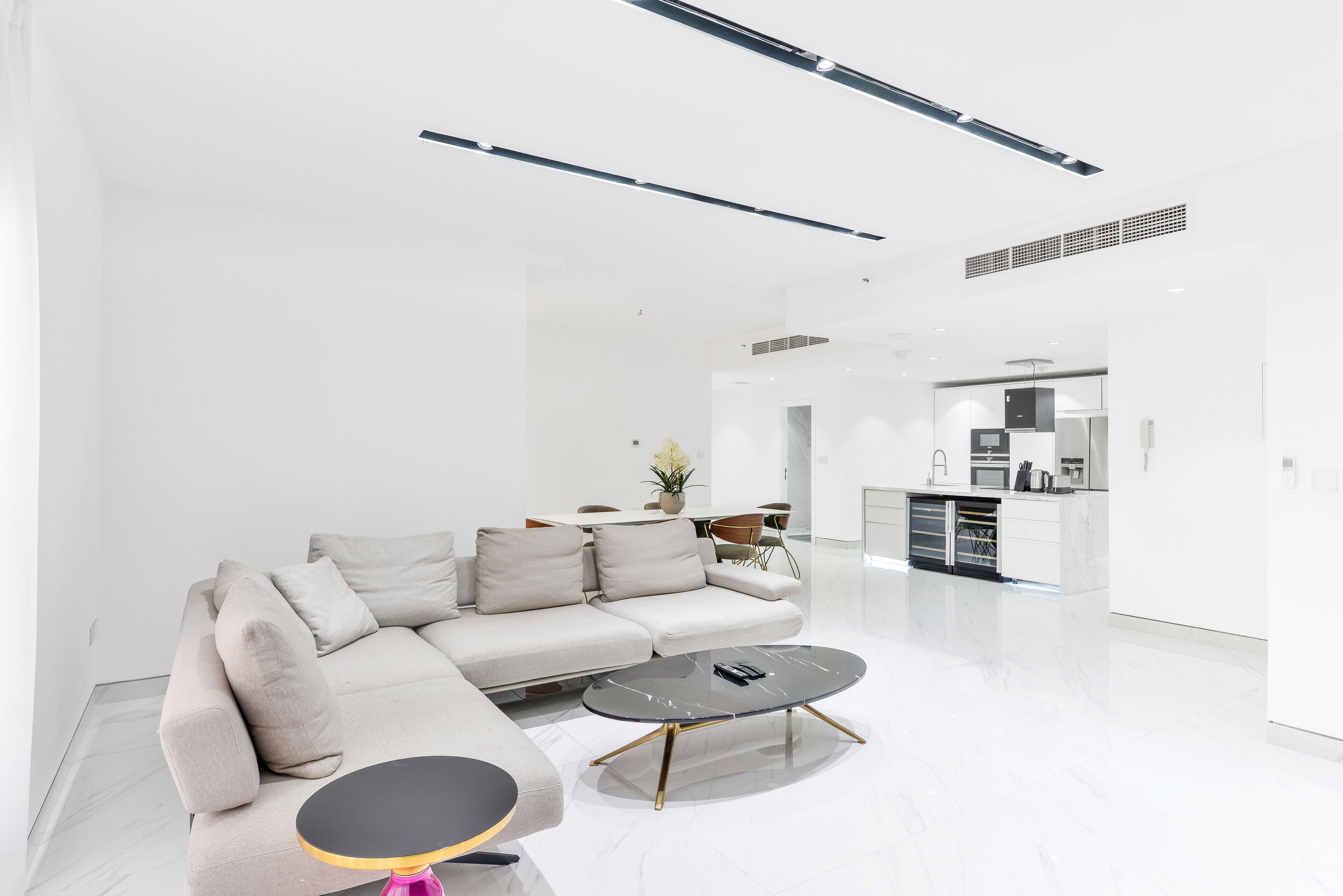 A modern living room with a sectional sofa, a round coffee table, and a dining area in the background.