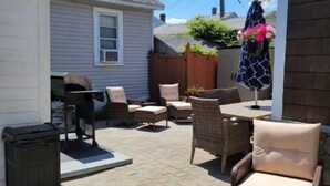A patio area with wicker furniture, a trash bin, and a wooden fence. - Cottage 200ft From Beach and Boardwalk ! (Hampton)
