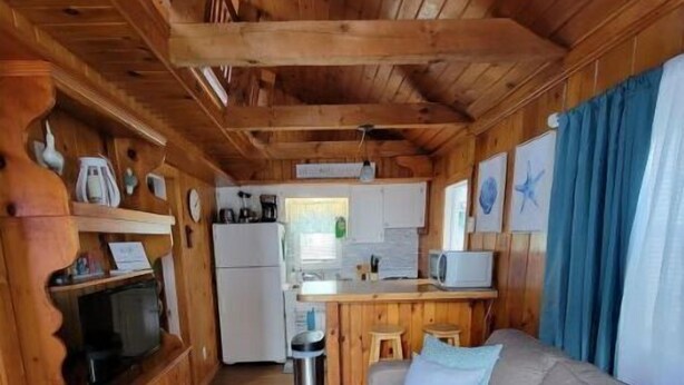 A wooden cabin interior with a kitchen, a sofa, and a television. - Cottage 200ft From Beach and Boardwalk ! (Hampton)