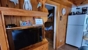 A wooden interior with a television on a built-in cabinet, a refrigerator, and a trash can. - Cottage 200ft From Beach and Boardwalk ! (Hampton)
