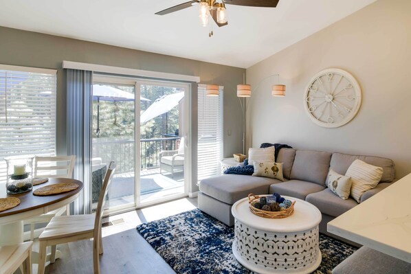 A modern living room with a sofa, a dining table with chairs, a coffee table, and a large window with blinds. - Updated Lake Almanor Retreat w/ Patio & Grill! (Westwood)