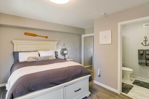 A bedroom with a bed, a bedside table, a nightstand, a mirror, a door, and a bathroom visible through an open door. - Updated Lake Almanor Retreat w/ Patio & Grill! (Westwood)