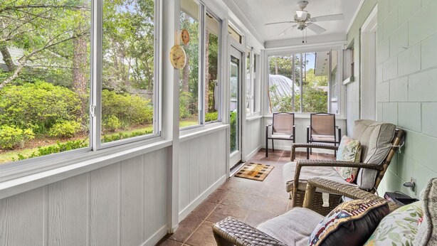 Eine überdachte Veranda mit großen Fenstern, Korbmöbeln und einem Deckenventilator.
