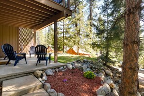 Un espacio de estar al aire libre con techo, sillas Adirondack, un hogar de piedra y vistas a un área boscosa.
