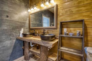 Une salle de bain avec un meuble-lavabo en bois, deux vasques, un grand miroir et une étagère contenant des articles de toilette.