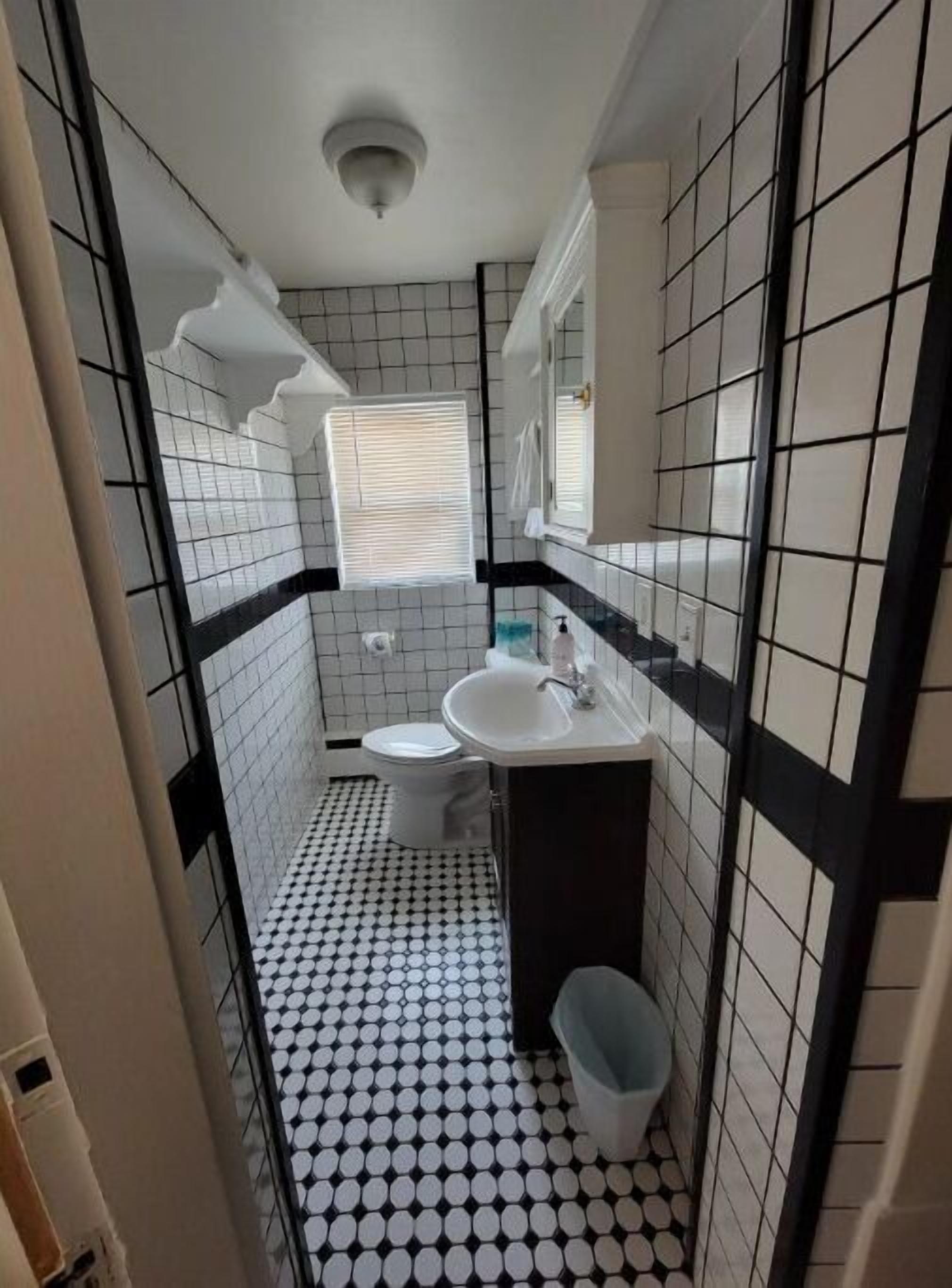 Un baño pequeño con inodoro, lavamanos y espejo. El suelo tiene un diseño de cuadros blancos y negros.