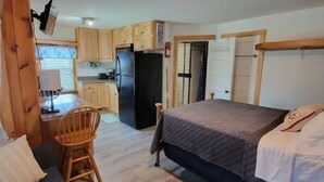 Een compacte kamer met een bed, een klein bureau, een stoel en een kitchenette.