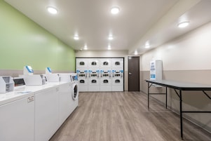 Un cuarto de lavandería con varias lavadoras, una lavadora industrial y una mesa con dispensador de jabón.