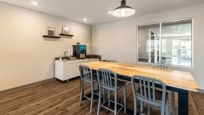 Una cucina moderna con un piano di lavoro in legno, forno integrato e macchina del caffè. Si vedono due quadri appesi al muro, un armadietto bianco e una finestra che dà su un parcheggio.