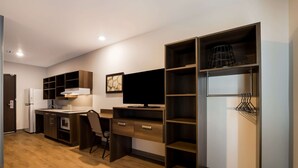 Una cucina compatta con frigorifero, microonde e fornelli, un'area pranzo con una sedia e una TV fissata al muro.