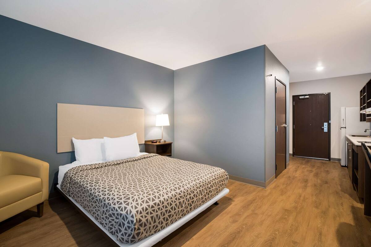 A hotel room with a bed, bedside table, lamp, and a small sofa.