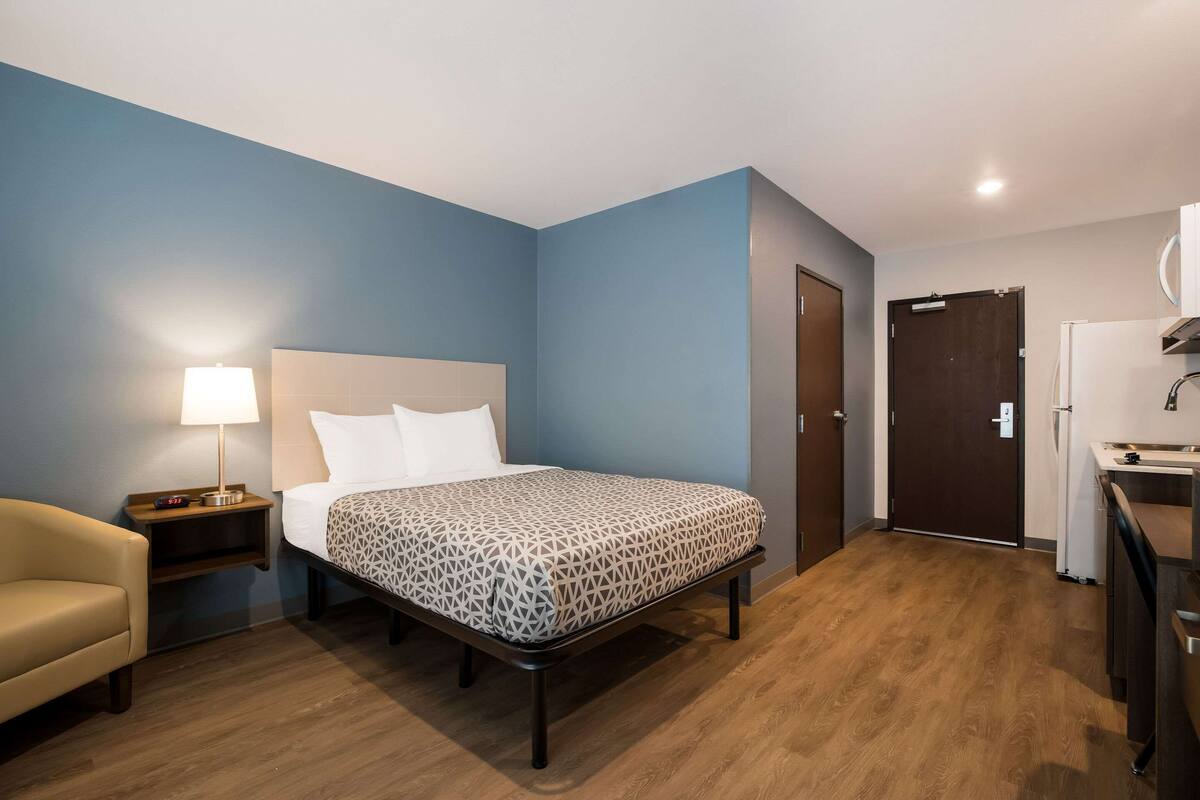 A hotel room with a bed, bedside table, lamp, and a small seating area.