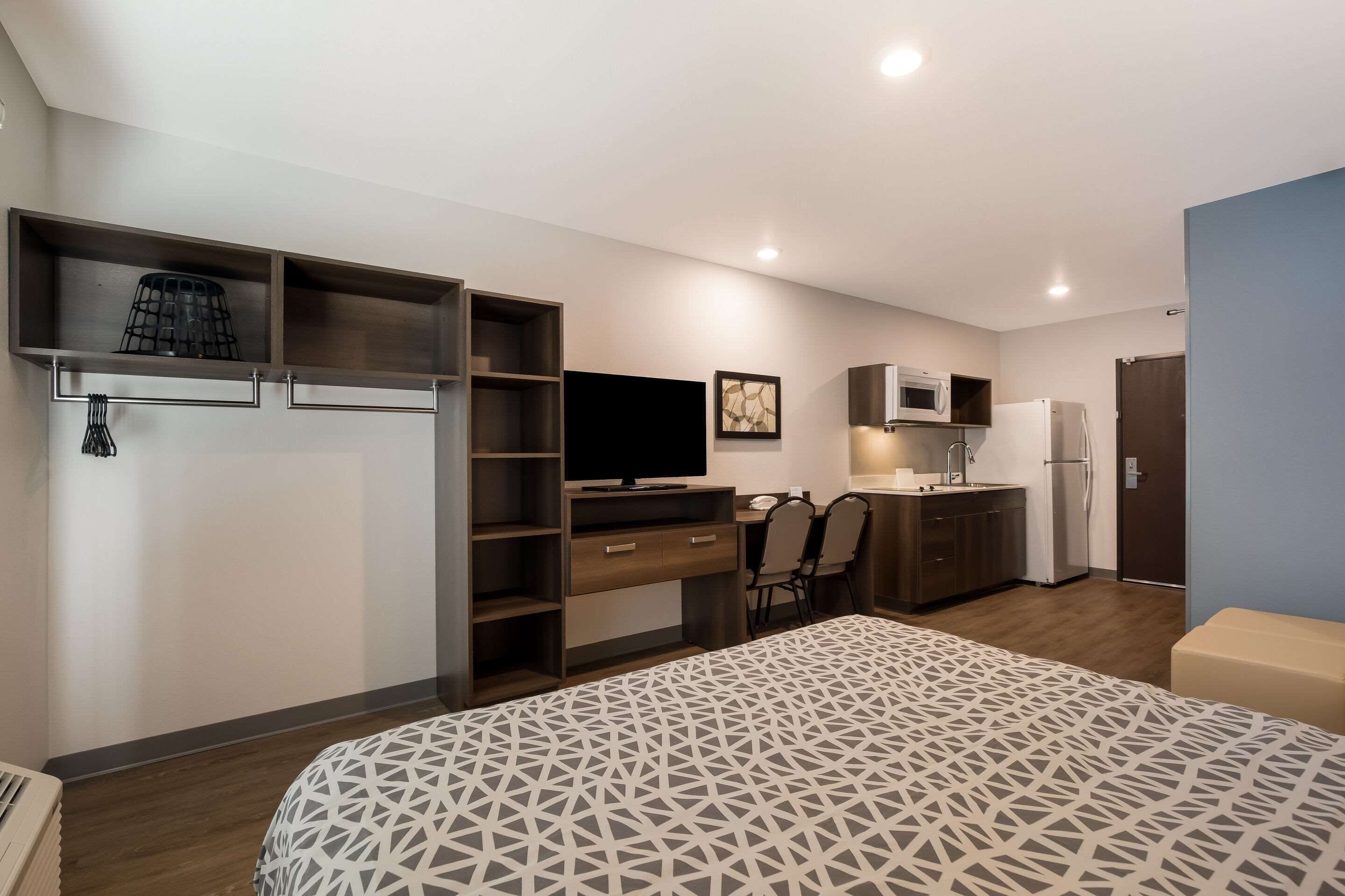 Une chambre moderne comprenant un lit, une armoire intégrée, un bureau et un coin cuisine.