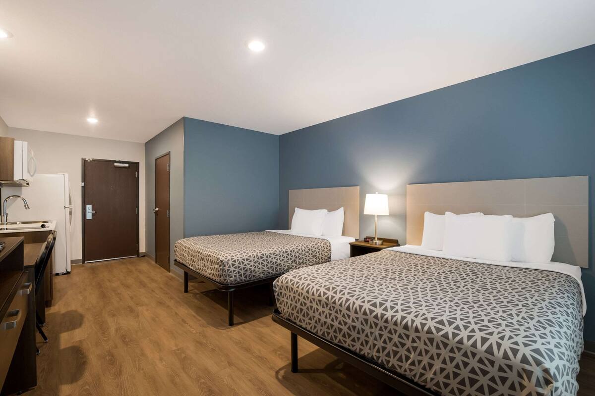 A hotel room with two beds, a desk with a sink, and a door.