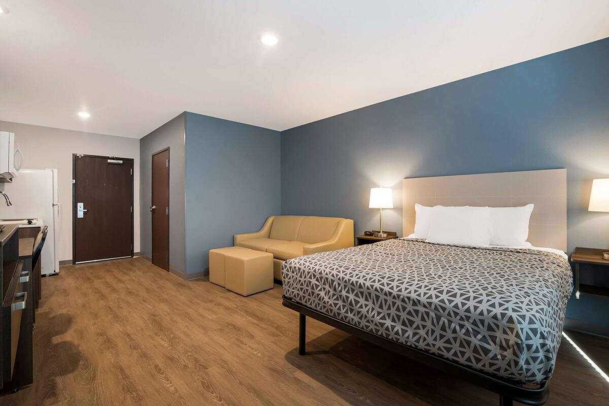 A hotel room with a bed, a sofa, a desk, and a door.