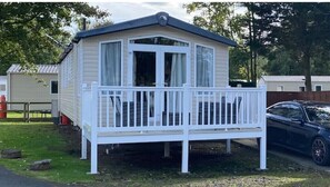 Situated in a grassy area with trees, this mobile home features a balcony and a convenient parking space nearby.
