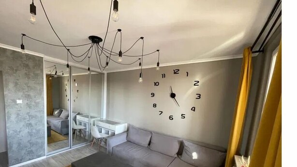 A modern living room with a large wall clock, a sofa, a coffee table, and a desk with chairs. - Silesia City Center Shopping Mall – 2,6 km (Katowice)