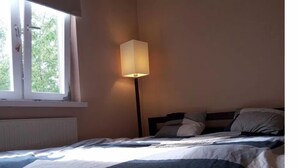 A bedroom with a bed, a bedside lamp, a window, and a radiator. - Silesia City Center Shopping Mall – 2,6 km (Katowice)