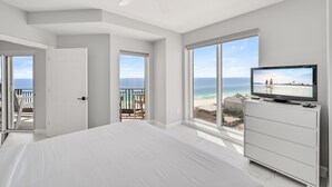 A bedroom with a large bed, a TV on a dresser, and a balcony with a view of the ocean. - Westwinds 4786 (Miramar Beach)