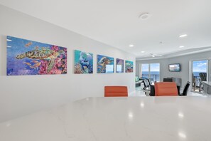 Un interior moderno con una larga recepción, una zona de estar con sillas naranjas y una pared grande con arte colorido.