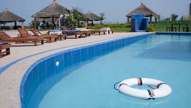 A swimming pool with lounge chairs and thatched-roof structures. - Lovely 13-bed Complex on Cape Point Beach, Bakau - Bojang River Lodge (Bakau)