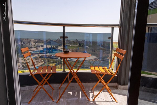 Ein Balkon mit Tisch und zwei Stühlen, mit Blick auf einen Ferienort mit Gebäuden und einem Pool.