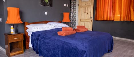 A bedroom with a bed, two bedside tables, a nightstand, a door, and a window with curtains.