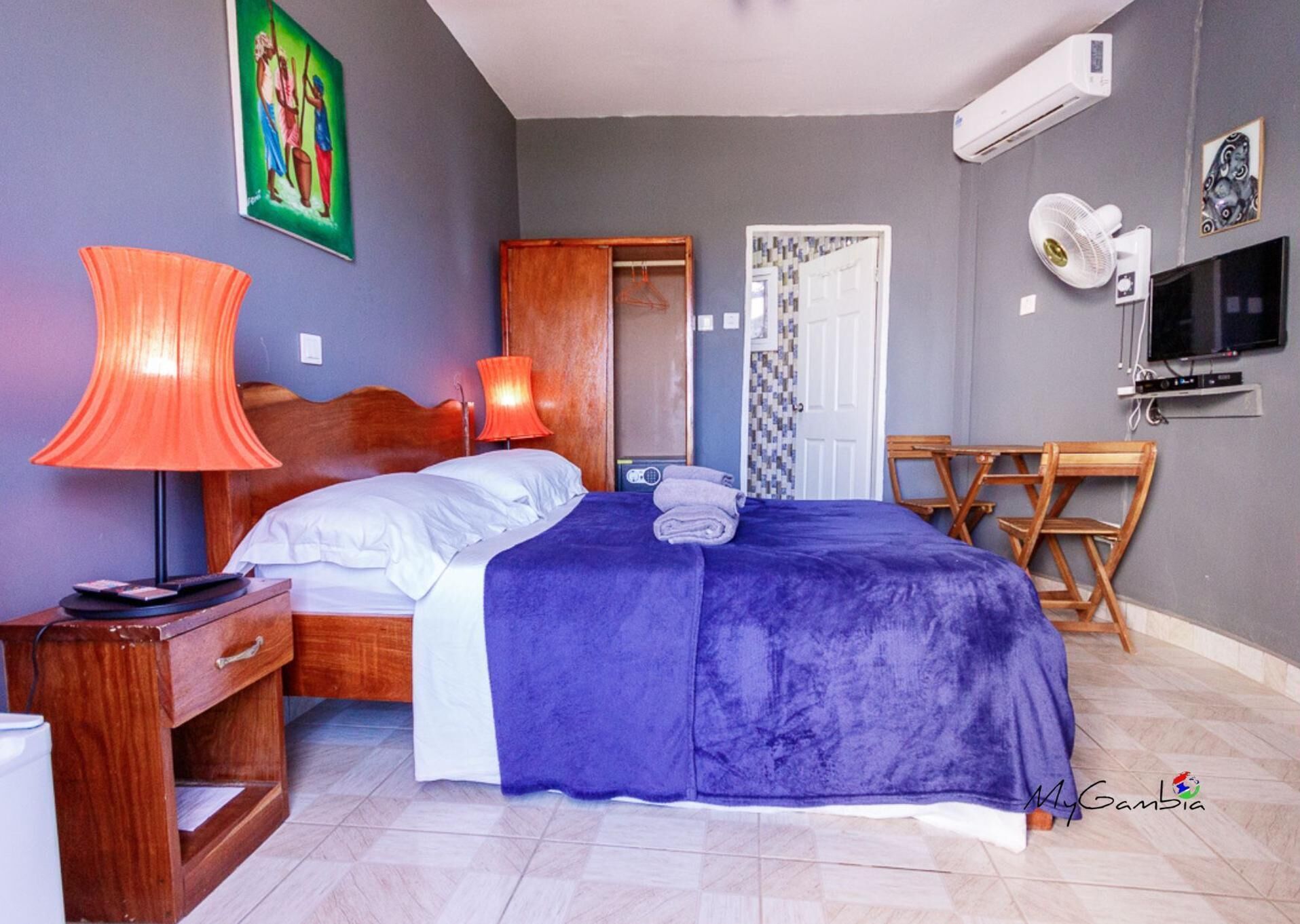 A bedroom with a bed, a nightstand, a lamp, a TV, and a chair.