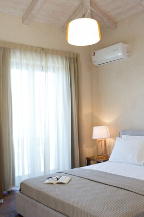 A hotel room with a bed, an air conditioner, a lamp, and a window with curtains.