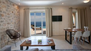 A living room with a stone wall, a wooden table, a sofa, and a balcony with a view of the sea. - Superior Two-Bedroom Villa (Lefkada)