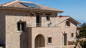 A stone building with a tiled roof, a balcony with hanging flowers, and a small window. - Superior Two-Bedroom Villa (Lefkada)