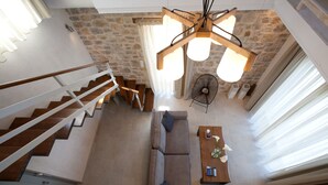 A spacious living area with a stone wall, a wooden staircase, a sofa, a coffee table, and a fan. - Superior Two-Bedroom Villa (Lefkada)
