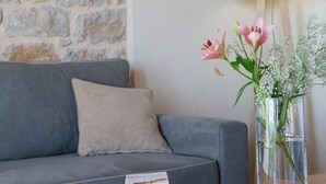 Un soggiorno con parete in pietra, un divano grigio, un tavolino in legno con libri e un vaso con fiori.