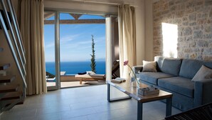 Un soggiorno moderno con un divano, un tavolino da caffè e vista sul mare attraverso una porta in vetro.
