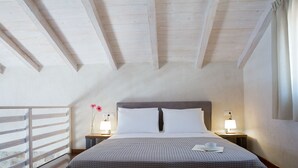 Una camera da letto con soffitto in legno, un letto con biancheria bianca, due lampade da comodino e un comodino.
