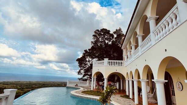 A resort with a pool, outdoor seating, and a view of the ocean. - El Castillo Tropical (Cabrera)