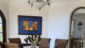 A dining area with a round table surrounded by wicker chairs, a chandelier, and a colorful abstract painting on the wall. - El Castillo Tropical (Cabrera)
