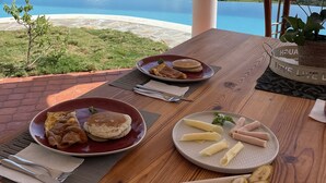 A table with breakfast plates, a view of a coastal landscape, and a wooden table. - El Castillo Tropical (Cabrera)