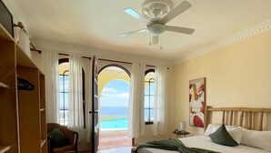 A bedroom with a bed, a chair, a wardrobe, and a view of the ocean. - El Castillo Tropical (Cabrera)