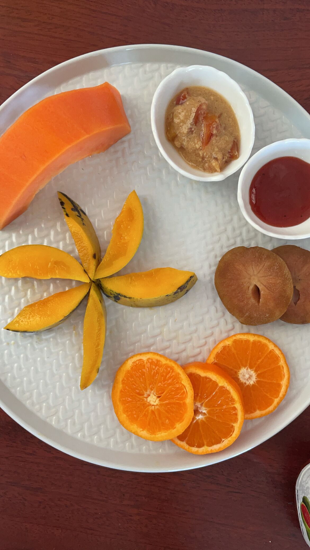Un piatto con papaya a fette, mango, spicchi d'arancia e due piccole ciotole di chutney.