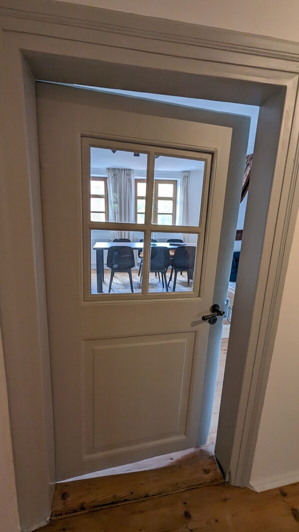 A white door with a glass panel, leading to a dining area with a table and chairs.