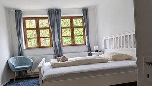 Un dormitori amb un llit, una cadira, una finestra amb cortines i un radiador.