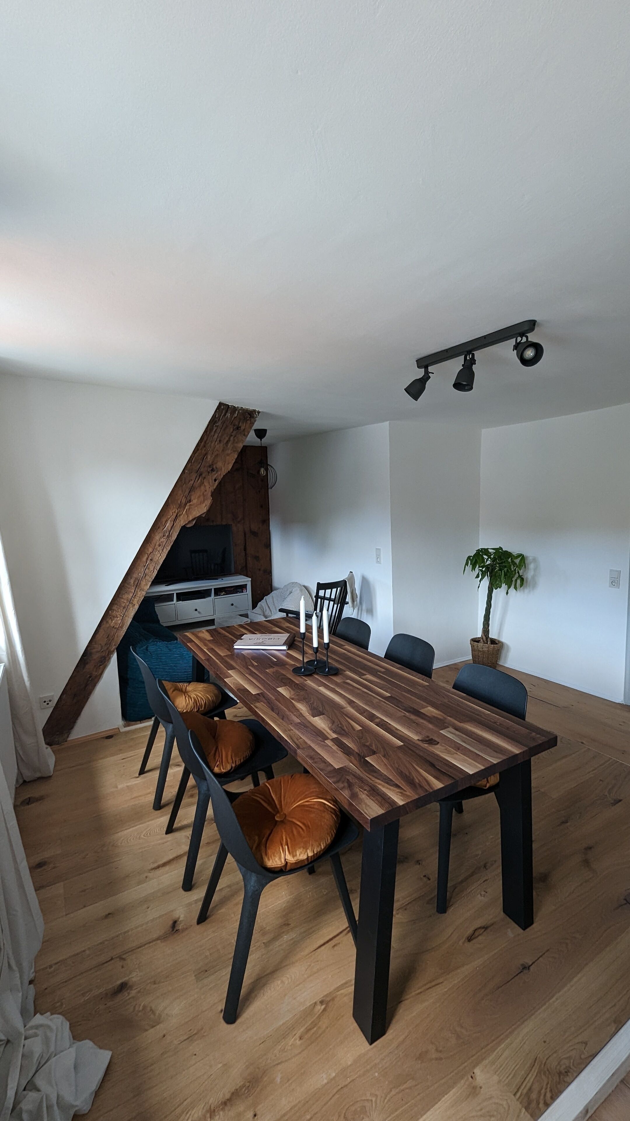 A dining area with a wooden table and chairs, a kitchen in the background, and a staircase.