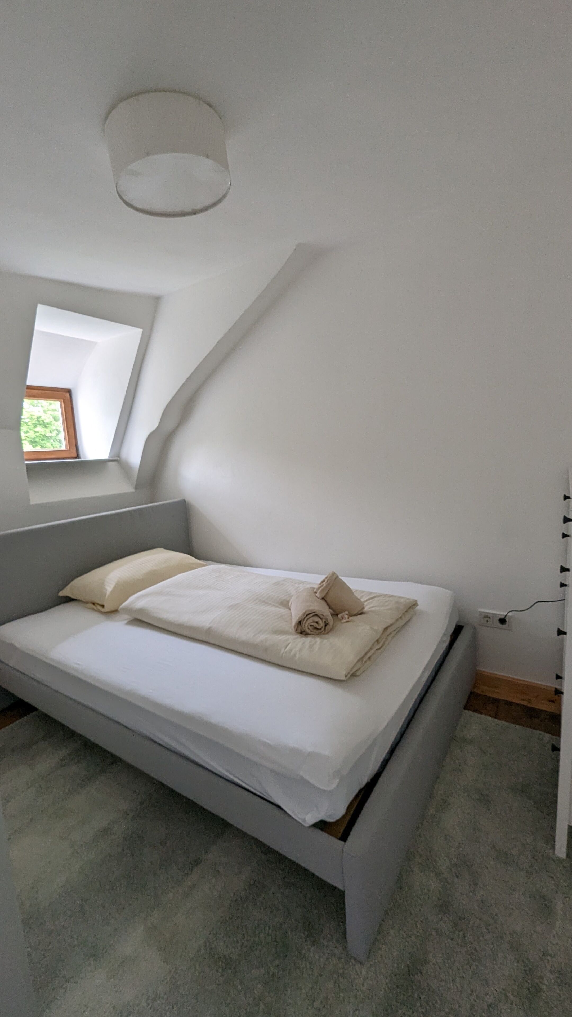 Un dormitorio con cama, ventana y lámpara en el techo.