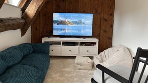 Una habitació acollidora amb sostre de fusta, una televisió sobre un moble blanc, un sofà color aguamarina, una cadira blanca i un otomà petit.
