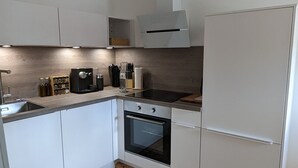 Una cuina moderna amb armaris blancs, forn integrat i campana extractora d'acer inoxidable.