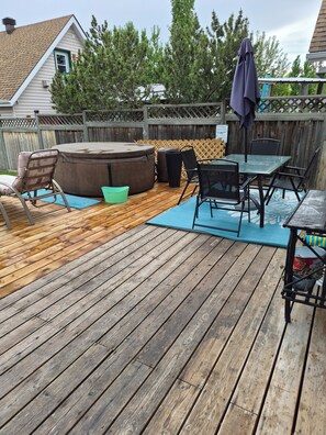 A wooden deck with a hot tub, outdoor seating, and a table with chairs. - Beach Retreat with Hot Tub | 1 Block to Beach | Free Parking (Sylvan Lake)