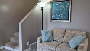 A living room with a staircase, a patterned sofa, and a framed artwork on the wall.